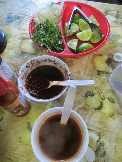 (Top to bottom) Condiment bowl of onion, cilantro and lime; chile sauce; birria de chico consommé
